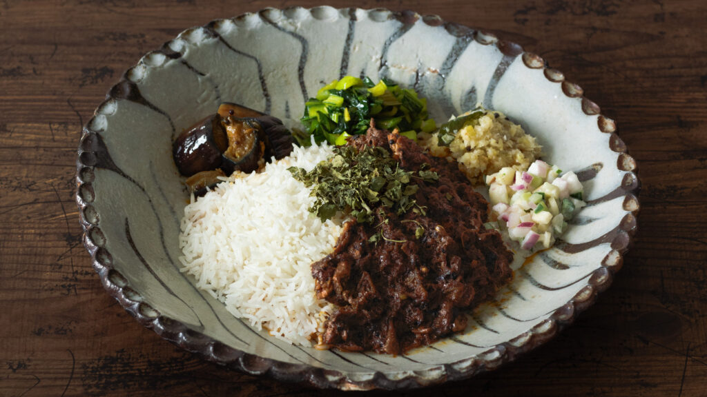 野菜や肉の持つ水分だけで鶏肉が柔らかくなるまで煮込まれた具材とスパイスが絶妙に溶け合い、うまみが凝縮した無水チキンカリー。ライスとカレーの周りの副菜を混ぜることで味の変化も楽しめる。